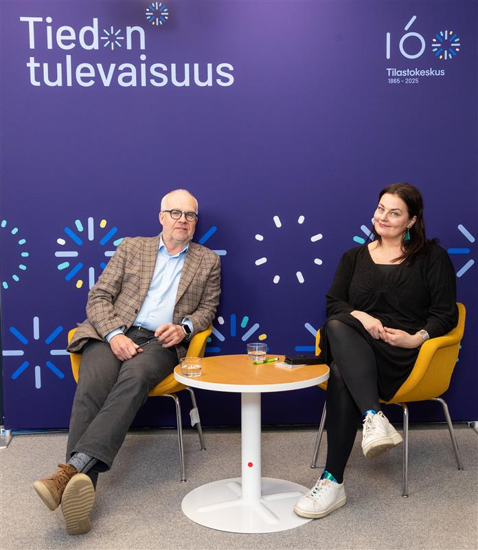 Tilastokeskuksen pääjohtaja Markus Sovala ja valtiosihteeri Kristiina Kokko istuvat sinisen taustan edessä. Taustassa lukee "Tiedon tulevaisuus".